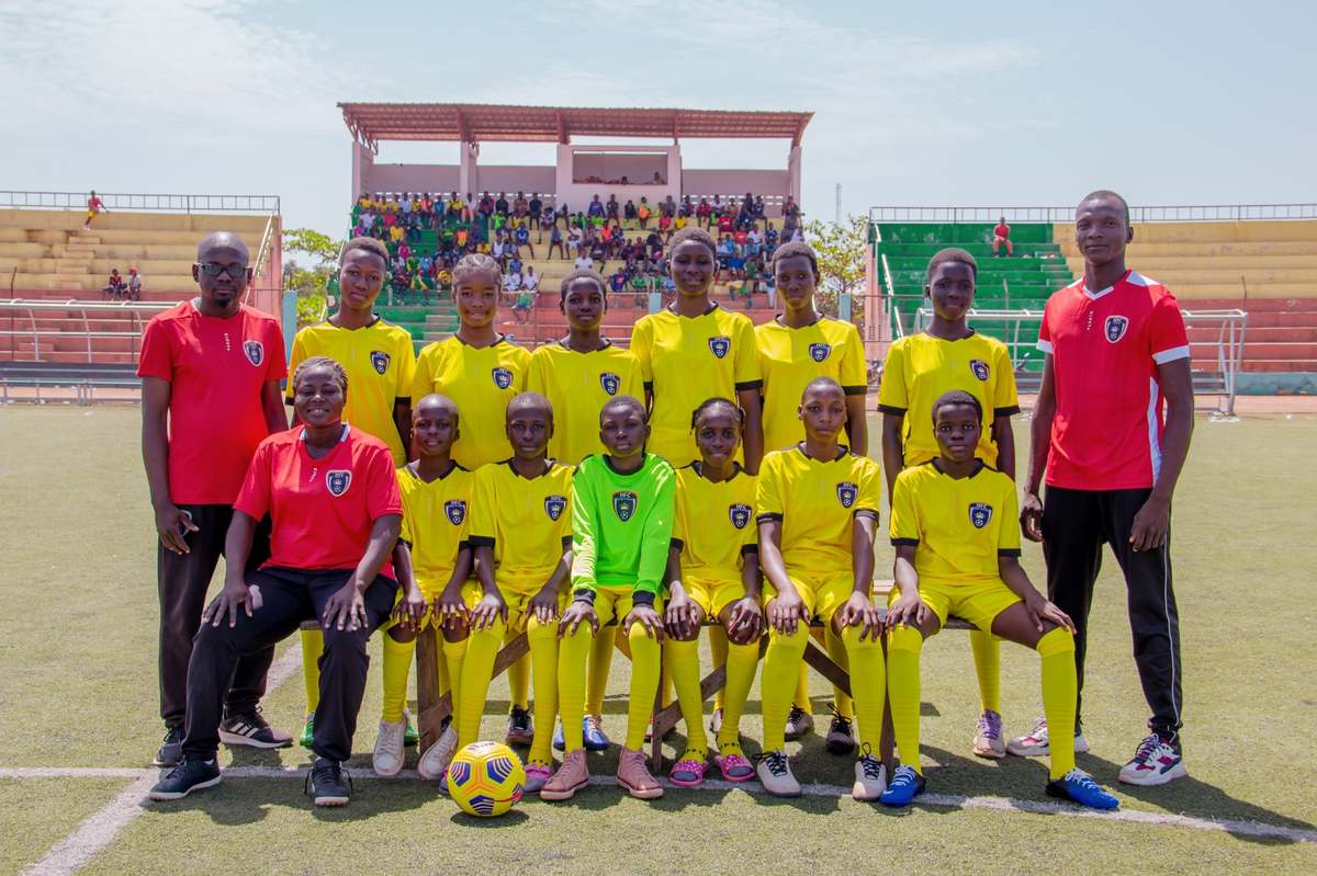 La photo officielle de l'équipe filles de Hooli Académie en maillot jaune, avec trois encadrants, au stade.